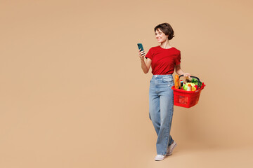 Full body young happy woman wear red t-shirt casual clothes hold basket bag with food products use...