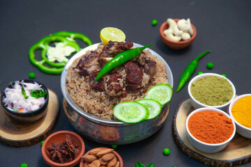 mutton biryani, beef biryani, chicken biryani along with cucumber slice, onion, onion raita, capsicum, cashews, almond, green peas, chili powder, coriander powder and spices on silver bowl