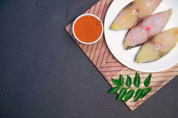 Fishy fry, Seer fish fry, salmon fish fry, raw fish along with lemon, ginger, garlic, chili powder and spices on white bowl and wooden cutting plate