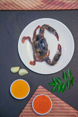 crab dried fry, blue crab fry, cooked crab along with garlic, mint leaves, chili powder, turmeric powder and spices on white plate in a wooden texture 