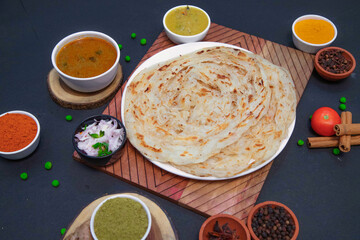 Kerala Malabar parotta, big parotta along with onion or creamy onion raita, lemon, Star anise, clove, chicken gravy and spices on white plate 