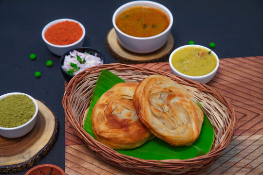 Poricha parotta, ghee parotta along with onion or creamy onion raita, lemon, Star anise, clove, chutney, chicken gravy and spices on bamboo plates or wooden plates
