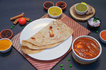 chapati along with onion or creamy onion raita, lemon, tomato, Star anise, green peas, chicken gravy, mutton gravy and spices on white plate