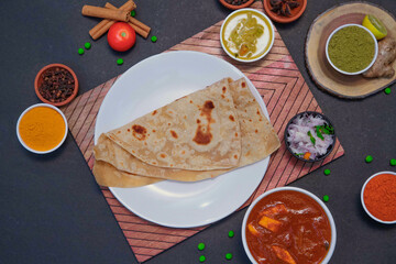 chapati along with onion or creamy onion raita, lemon, tomato, Star anise, green peas, chicken gravy, mutton gravy and spices on white plate