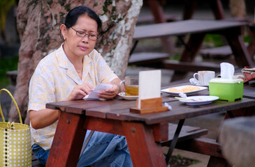 Fototapeta premium Woman sitting on a wooden bench in a garden restaurant, enjoying her afternoon ginger tea