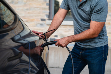 Obraz premium Close up of man plugging EV charger into electric vehicle outside.