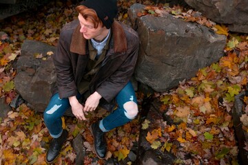 A man wearing a beanie pauses on rocks amidst autumn leaves,