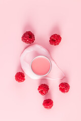 A round cosmetic jar with a delicate lip balm stands on a sample of a delicate liquid lip skin balm among ripe raspberries. Vertical top view.