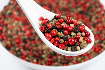 Different varieties of peppercorns, red, green, black and white peppers in a spoon