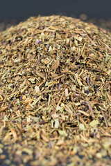 Pile of chopped dry basil seasoning on a black background.