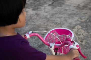 child rides her bike with a pink basket attached to the handlebars in the outdoor setting, while the kid enjoys her playful journey on the pavement.