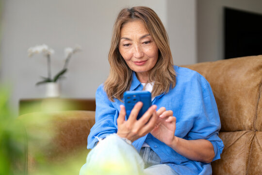 Woman in casual attire engaging with her smartphone while relaxing on a cozy couch in a bright, modern living space