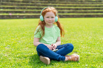 Fototapeta premium A young girl with headphones enjoys a peaceful moment on the green lawn during a sunny day in the park