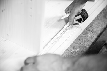 Carpenter taking measurement of wooden plank using tape measure.
