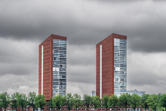 Two twin red brick towers rise prominently, set against a backdrop of ominous gray clouds, representing stability and monumental presence amid brooding weather conditions.
