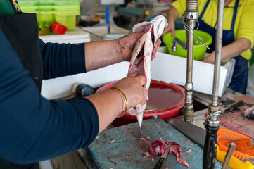 A person skillfully filleting fish at a bustling market stall during the morning hours.
