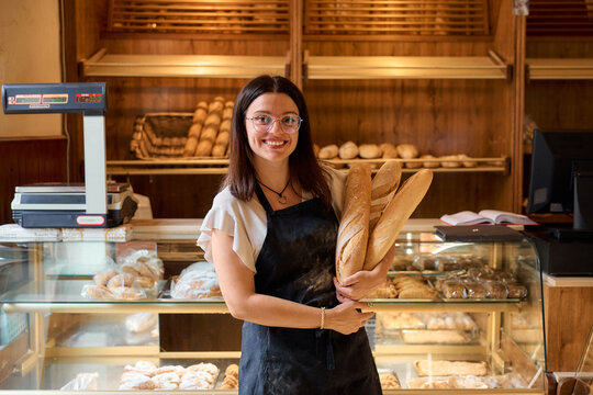 Young baker holding fresh bread loaves in a cozy bakery setting
