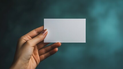 Fototapeta premium Hand holding blank business card with a blurred teal background.