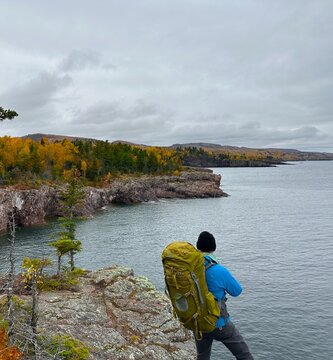 solo man backpacker  hiker hikes along a cliff over lake superior, minnesota, cathcing a view of the fall colorful yellow trees