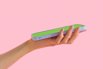 A vibrant hand holding a sleek smartphone against a pastel pink backdrop during a bright afternoon