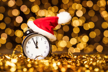 Christmas alarm clock with Christmas cap on New Year's bokeh background