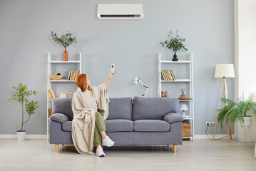 Girl wrapped in blanket switching on, off air conditioner, blowing warm air room temperature control, adjust optimal performance, home environment, providing ideal climate heating system in cold flat