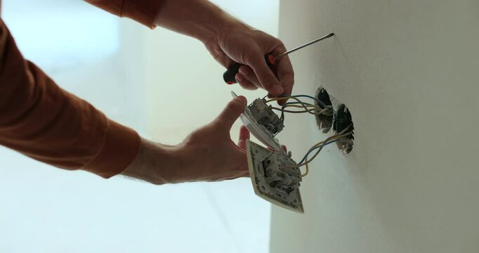 Professional electrician working on a home electrical system. Close up man installing a wall socket at new apartment or house.
