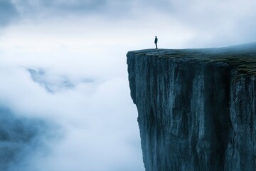 A person is standing on a cliff overlooking a cloudy sky. Concept of solitude and contemplation, as the person is alone on the edge of the cliff. The cloudy sky adds to the mood of the image