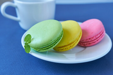 Colorful macaroons in white plate on blue tablecloth.