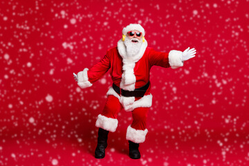 Full length x-mas photo of pensioner old man white beard plane dance newyear party wear santa costume gloves coat belt sunglass headwear earphones black boots isolated red color background