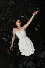 A woman with dark hair wearing a white dress and floating in the dark water