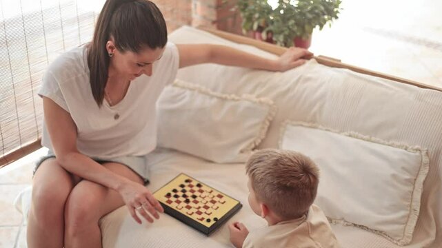 Caucasian mother playing checkers with her son on a couch