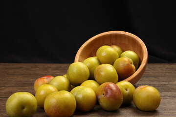 Ripe sweet small mini plum green maroon on rustic wooden table bowl black background