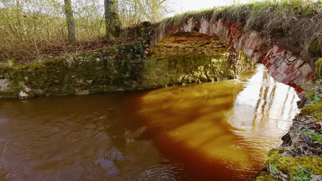Historic stone arch bridge over Kujas river in Latvia reflecting on the surface of a gently flowing river below