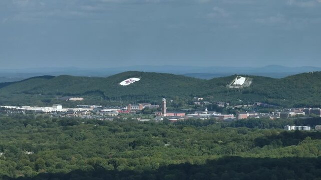Aerial wide shot of american town surrounded by green nature in Virginia. Tower and historic buildings in Timberlake, USA. Green hills in background.