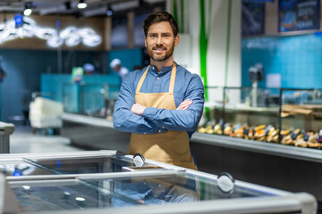 Store employee with apron displaying confidence and professionalism in supermarket seafood section. Background includes fresh seafood counter and modern grocery store setting creating atmosphere
