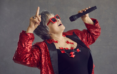 Senior fashionable woman star singing into microphone close-up. A woman in red glasses and clothes...