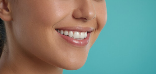 Obraz premium close-up profile shot of a young woman’s bright smile, showcasing her white teeth against a smooth, turquoise background, emphasizing dental hygiene and oral health