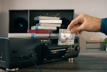 Male hand loading audio tape cassette into vintage music player. Prepared listening room with a nostalgic touch, showcasing a cassette recorder and high-quality audio equipment