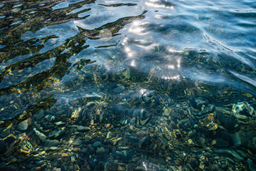 Underwater pebble backgrounds. Colorful stones sea bottom and sea fish in the sun rays. View from above through clear water. Seascape wallpaper texture.