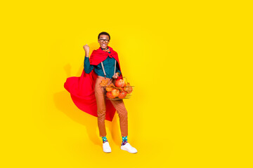 Full body portrait of nice elegant young man hold halloween pumpkin shop basket raise fist isolated on yellow color background