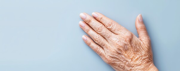 Fototapeta premium Elderly hand resting on a light blue surface, showcasing fine lines and textures of aging.