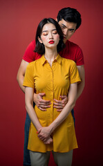 Naklejka premium An Asian couple, a man hugs his wife tenderly. Both are wearing jeans, she is wearing a yellow button-down shirt, and he is wearing a red shirt