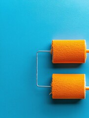Obraz premium Two orange paint roller brushes on a bright blue background.