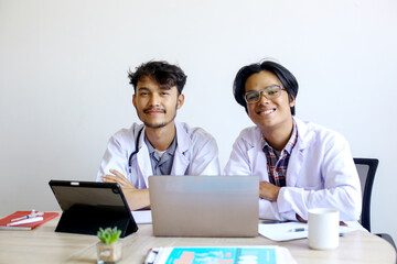 Obraz premium Portrait Of Young Asian Medical Students In Uniform Sitting On Working Desk And Looking At Camera Smiling
