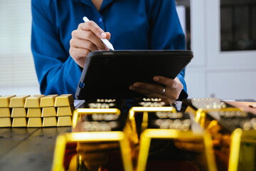 Gold bars in the hands of an Asian businesswoman at a desk in an office.