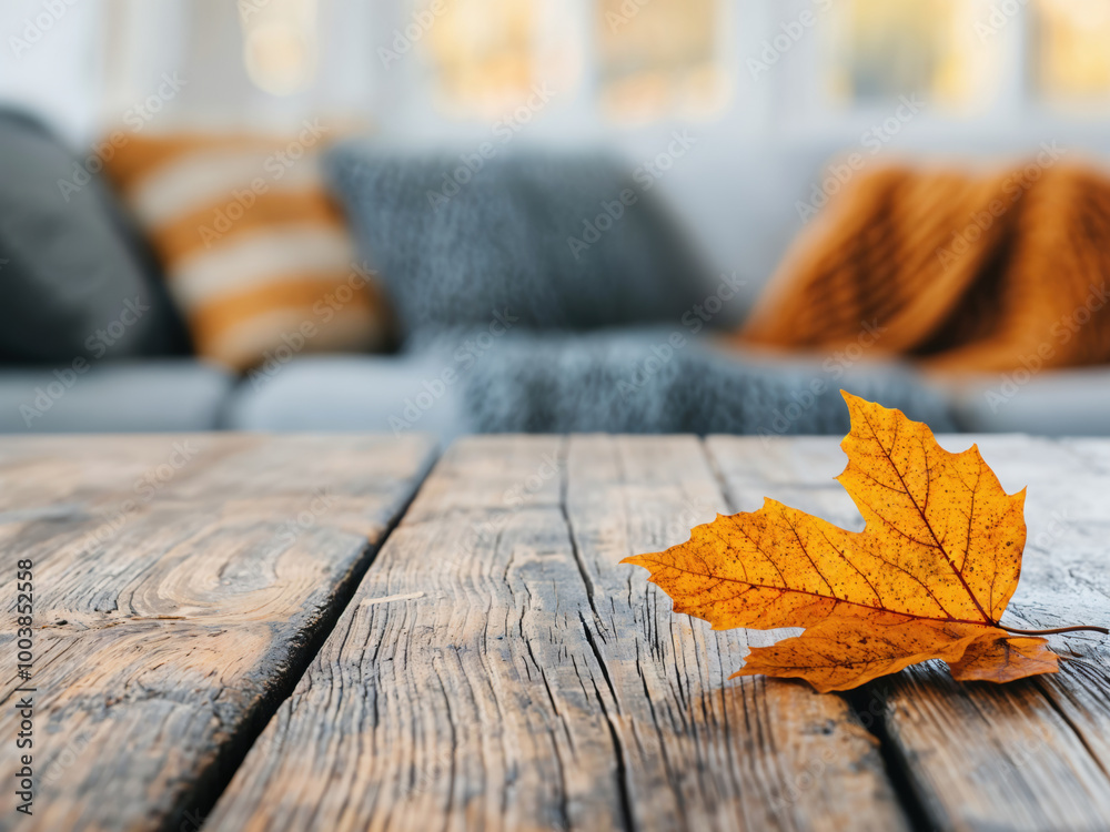 Aufkleber single yellow maple leaf lying on a wooden table with a sofa in the background