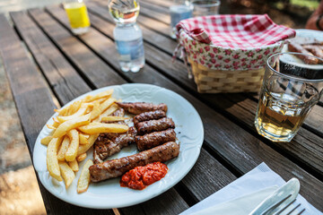 piatti con grigliata di carne mista e patate fritte, su un tavolo rustico in legno, insieme ad alcuni bicchieri, bottiglie d'acqua e un cestino per il pane, all'aperto, di giorno, in estate