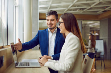 Young business man employee showing something to his colleague on the monitor screen on laptop on...