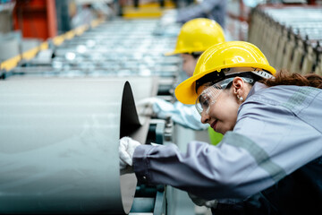 Female worker in safety uniform together work inspecting operation manufacturing Metal Roofing Sheet Machine in the factory metal sheet, Metalwork roof manufacturing and quality control process.